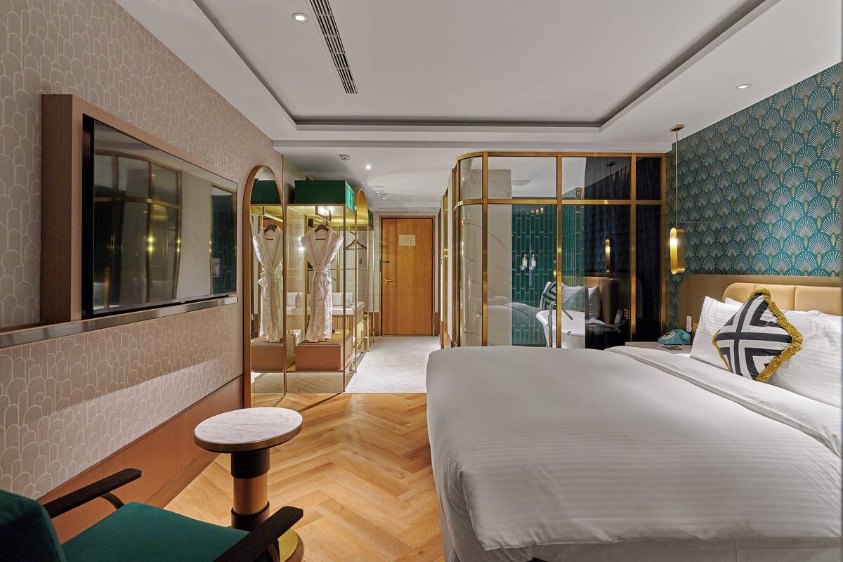 A hotel room with a large bed, a seating area with a round table, a mirror, and a wardrobe.