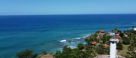 A coastal view with a lighthouse, ocean, and a small settlement with buildings and greenery.