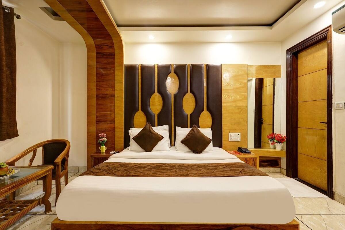 A hotel room with a large bed, wooden headboard, a wooden desk, and a nightstand with a vase of flowers.