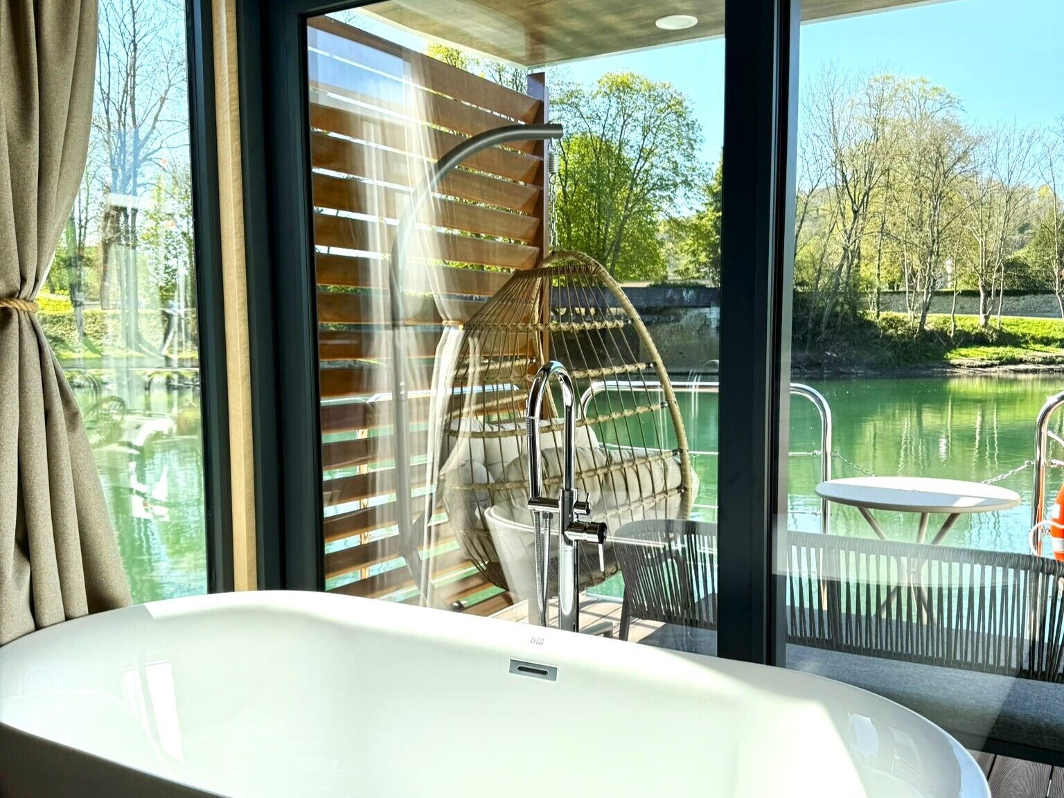 Un baño moderno con una bañera, una silla colgante y vistas a un lago.