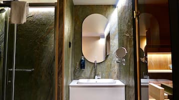 A bathroom with a marble wall, a white sink, a round mirror, and a handheld mirror.