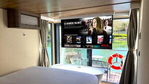 A modern hotel room with a large bed, a TV mounted on the wall displaying a movie, and a view of a lake through the window. - L'Escale Royale La Ferté-sous-Jouarre (La Ferté-sous-Jouarre)