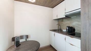 A compact kitchen with white cabinets, a dark countertop, a built-in stove, and a small dining table with a chair.