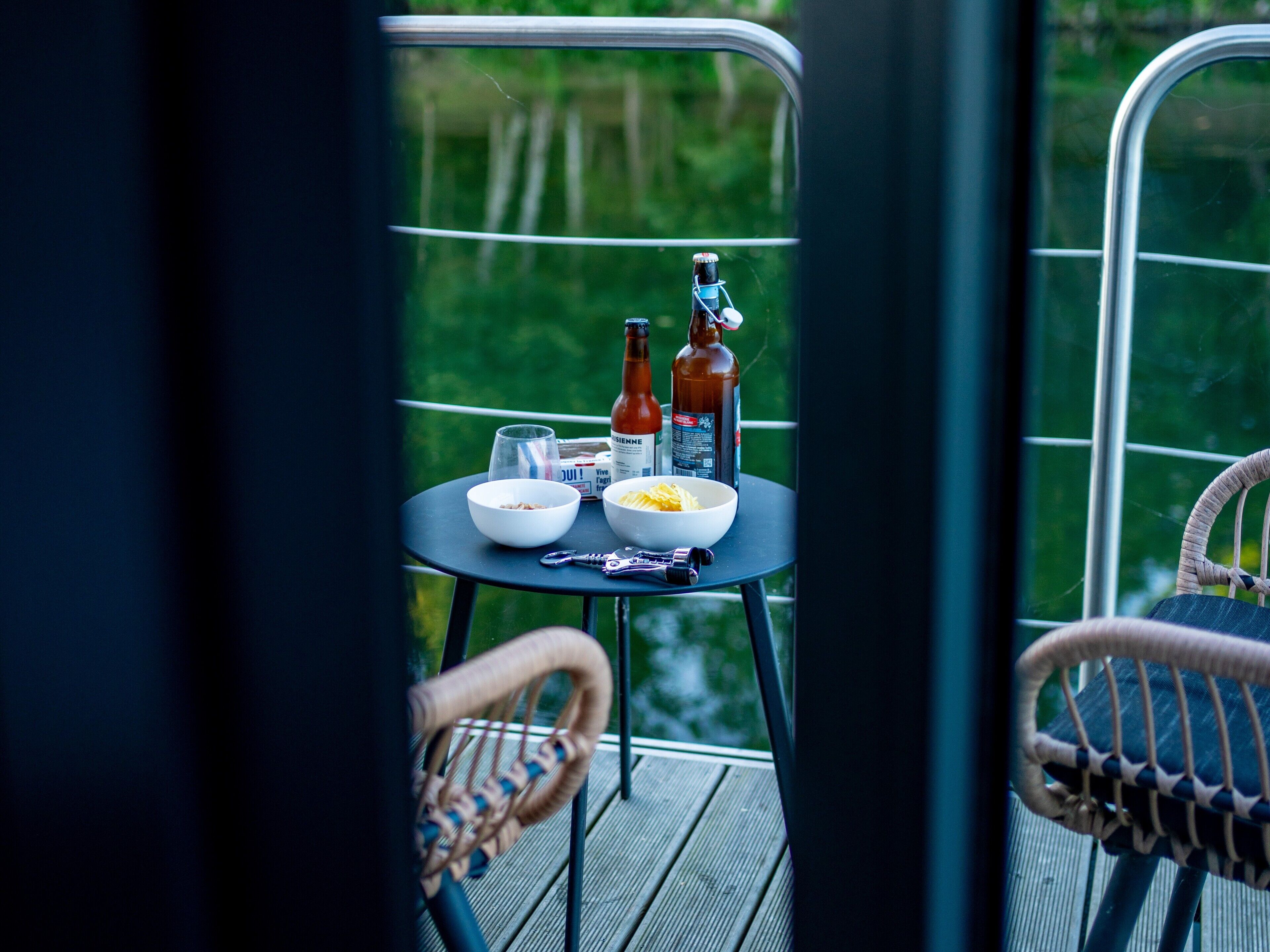 Ett bord med skålar, flaskor och ett glas på en balkong med flätade stolar.
