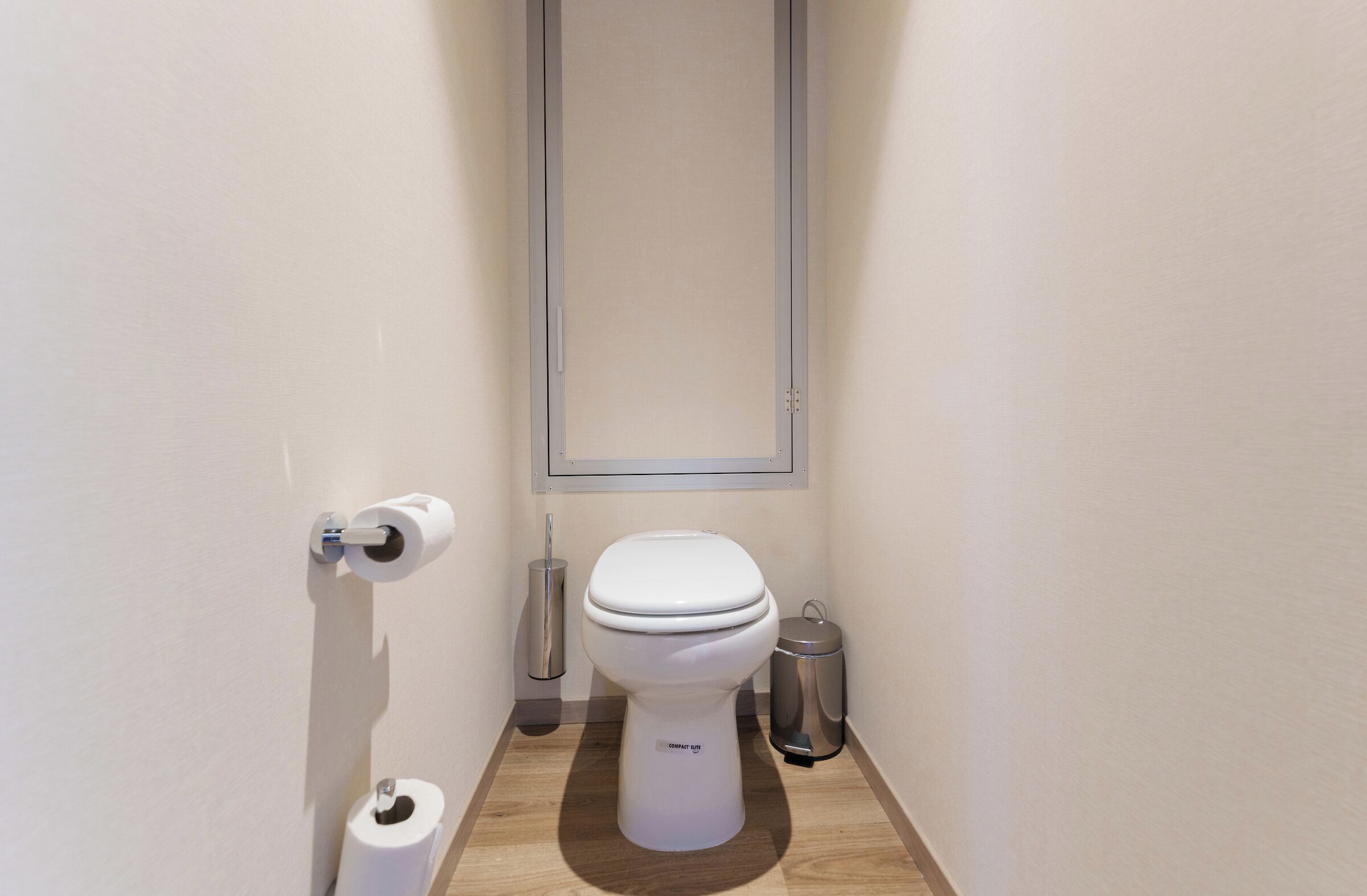 Un baño pequeño y moderno con inodoro, dispensador de papel higiénico y un cubo de basura.