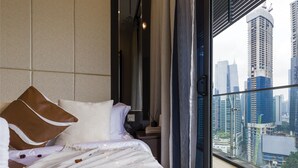 A modern hotel room with a large bed, a nightstand, a lamp, and a view of the city skyline through large windows. - Dorsett Kuala Lumpur by Five Senses (Kuala Lumpur)