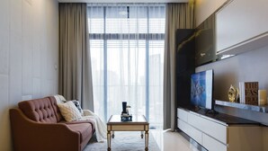 A modern living room with a sofa, a coffee table, a flat-screen TV, and a large window with sheer curtains. - Dorsett Kuala Lumpur by Five Senses (Kuala Lumpur)