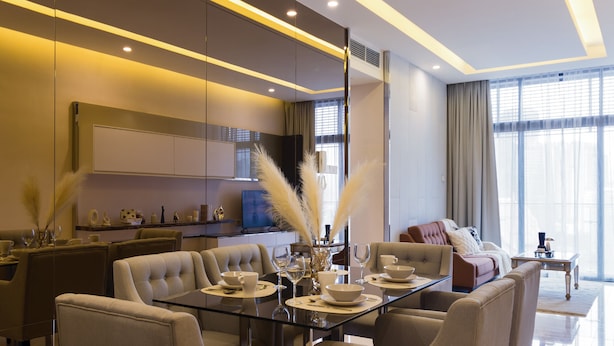 A modern living room with a glass dining table, comfortable seating, a large mirror, and a view of the outdoors through large windows. - Dorsett Kuala Lumpur by Five Senses (Kuala Lumpur)