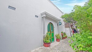 A narrow cobblestone street with a white building featuring a green door and potted plants. - Hotel O Yogyakarta near Jalan Malioboro formerly Malio Inn (Yogyakarta)
