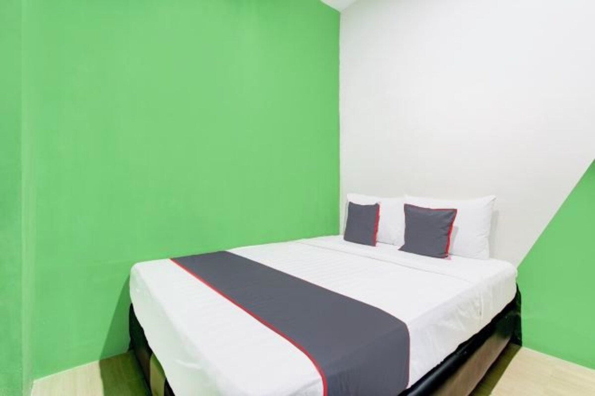 A single bed with a white and gray bedspread, two pillows, and a black headboard in a room with green walls.