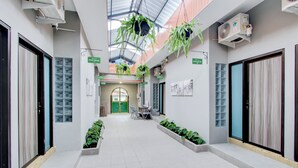 A modern indoor corridor with hanging plants, air conditioning units, and a central seating area. - Hotel O Yogyakarta near Jalan Malioboro formerly Malio Inn (Yogyakarta)