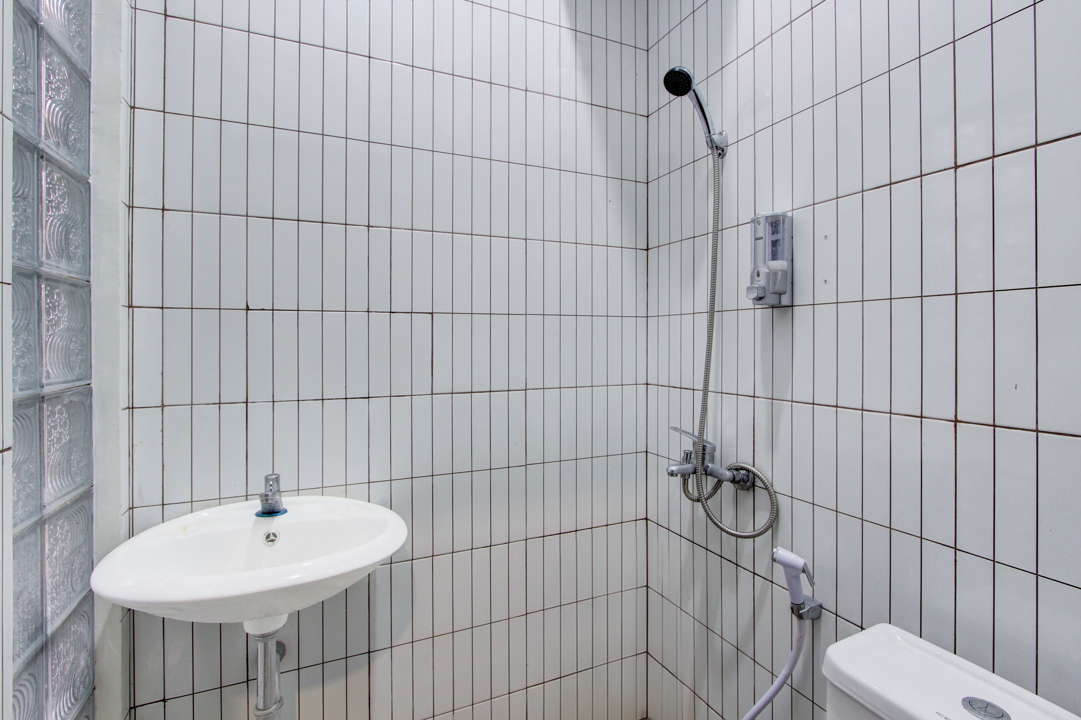 Ein Badezimmer mit weiß gefliesten Wänden, einem weißen Waschbecken und einer Dusche.