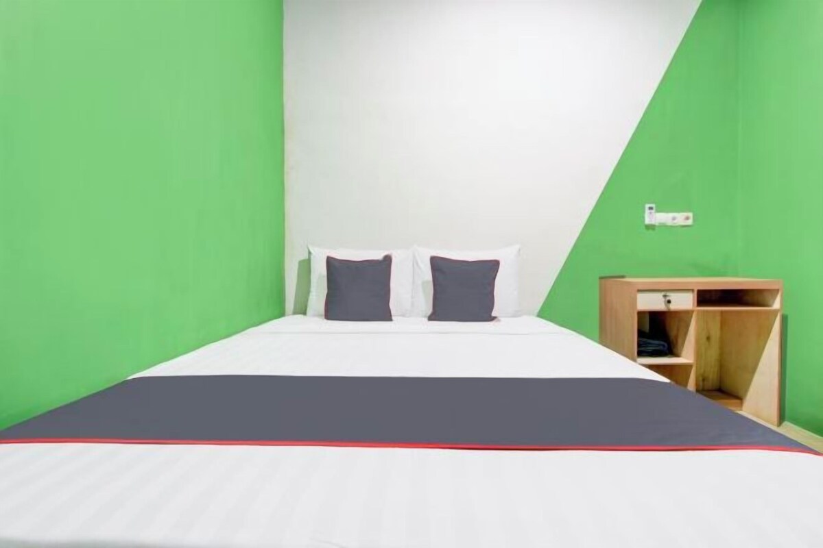 A bed with white bedding and two pillows, a wooden nightstand with a drawer, and a green wall.