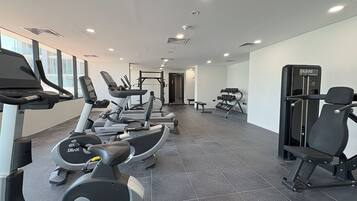 A modern gym with various cardio machines, weightlifting equipment, and a bench.