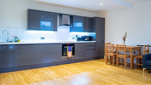 Una cocina moderna con armarios oscuros, una mesa de comedor de madera y una sala compacta.