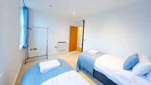 Habitación de hotel moderna con dos camas, un ventanal grande, un radiador y una puerta que da a otra habitación.