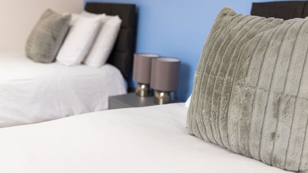 A hotel room with two beds, each with white bedding and grey pillows. There are two bedside tables with lamps. - Charlotte House: Prime Location Urban Nest – 2BED 2BATH (Ipswich)