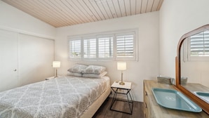 A bedroom with a bed, bedside tables, a dresser, a mirror, and a window with blinds. - Beautiful 1 Bed Beach Condo #224 1 Bedroom Condo by Sunset Shores Condominiums (Carpinteria)