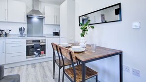 A modern kitchen with white cabinets, a stainless steel range hood, and a dining area with a wooden table and chairs.