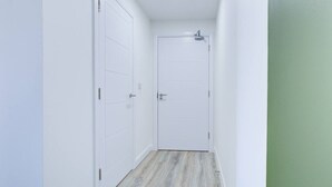 A narrow hallway with white walls and a wooden floor, leading to a closed door.