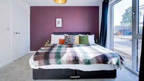 A modern bedroom with a large bed, purple walls, and a view of the outside.
