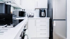 Une cuisine de taille réduite avec des meubles blancs, un réfrigérateur en acier inoxydable, un four à micro-ondes et une machine à café.