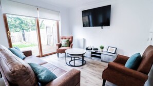 Un salon moderne avec un canapé en cuir marron, une table basse ronde et un fauteuil marron. Un téléviseur à écran plat est fixé au mur.