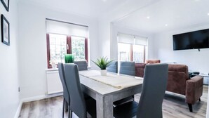 Un salon moderne comprenant un coin repas, un téléviseur à écran plat fixé au mur et une grande fenêtre avec des rideaux.