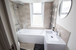 Un baño moderno con bañera, lavamanos y ducha. Hay una ventana que proporciona luz natural y un perchero en la pared.