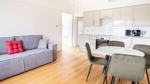 A modern apartment with a grey sofa, red cushion, and a dining area with chairs and a table. - 2BR Seaside Sanctuary in St Leonards on Sea Flat 5 (Hastings)