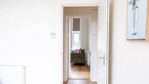 Un couloir menant à une pièce où se trouvent un lit, un radiateur et une fenêtre.