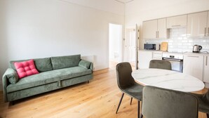 Un salon moderne avec un canapé vert, une table à manger ronde et une cuisine en arrière-plan.