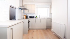 A compact kitchen with white cabinets, a microwave, a stove, and a window.