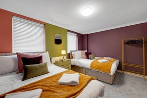 Two single beds with white linens and throw pillows, a large mirror, and a bedside table with a lamp.