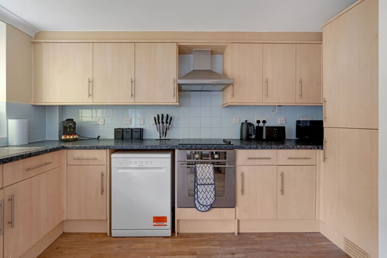 Une cuisine moderne avec des meubles de couleur bois clair, un lave-vaisselle, un four et un four à micro-ondes.