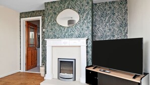 Ein Wohnzimmer mit Kamin, Fernseher auf einem Schrank und Wandtapete mit Muster.