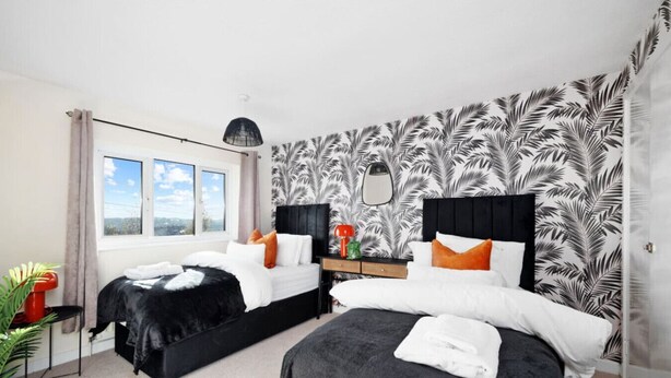 Ein Hotelzimmer mit zwei Betten, einem großen Fenster, Blick ins Freie, einer Pflanze und einem Spiegel an der Wand.