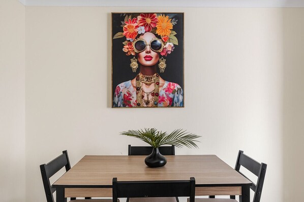 A dining area with a wooden table, four chairs, and a black vase with a plant.