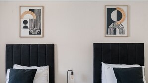Two beds with black headboards and white bedding, a nightstand with a lamp, and abstract art on the wall. - The Ipswich Snug Spacious 3BR Retreat FREE Parking (Ipswich)
