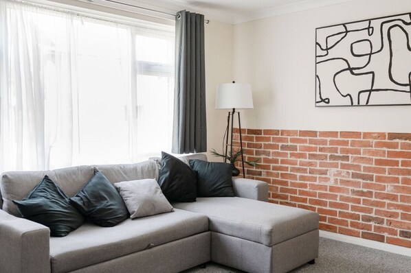 Una sala de estar con un sofá modular gris, una lámpara de pie y una pared de ladrillo.