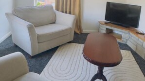 Una sala de estar con sofá, una mesa de centro y un televisor sobre una consola de piedra.