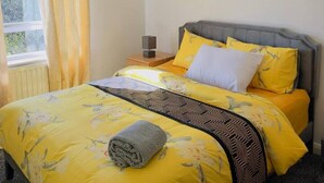 Un dormitorio con cama, mesita de noche, lámpara y ventana con cortinas.