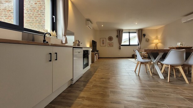 Een moderne keuken met een eethoek, met een groot raam, inbouwapparatuur en een visgraat parketvloer.