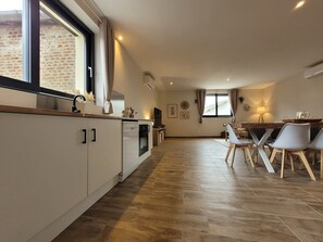 Une cuisine moderne avec un coin repas, dotée d’une grande fenêtre, d’appareils électroménagers intégrés et d’un parquet en bois disposé en chevrons.