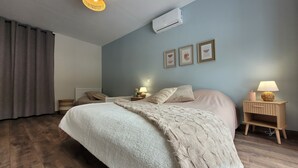 Een slaapkamer met een groot bed, een nachtkastje met een lamp, een wandairconditioner en een plafondlamp.