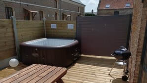 Een houten terras met een hottub, een barbecue en een picknicktafel.