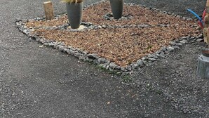 Een binnenplaats met een grindpad, twee plantenpotten en een bakstenen gebouw met grote ramen en een deur.
