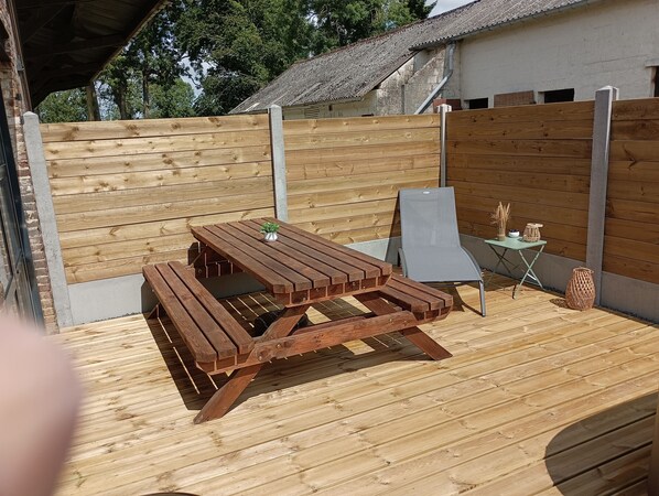 Une terrasse extérieure en bois, avec une table de pique-nique et un fauteuil de relaxation.