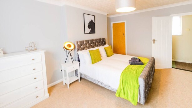 Un dormitorio con cama, lámpara de noche, cómoda y puerta.