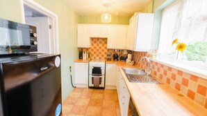 Cocina compacta con armarios blancos, refrigerador negro, salpicadero de azulejos y ventana con flores.